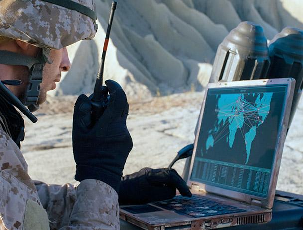 一个士兵一边用手持卫星收音机讲话，一边用笔记本电脑看地图